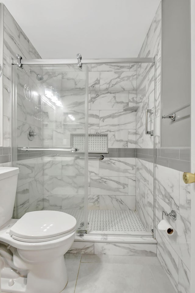 bathroom featuring tile walls, toilet, and a shower with door