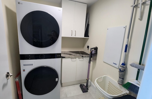 laundry room featuring stacked washer and dryer, light tile patterned floors, and cabinets