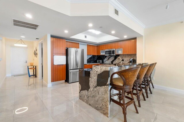 kitchen with crown molding, stainless steel appliances, a raised ceiling, decorative backsplash, and kitchen peninsula