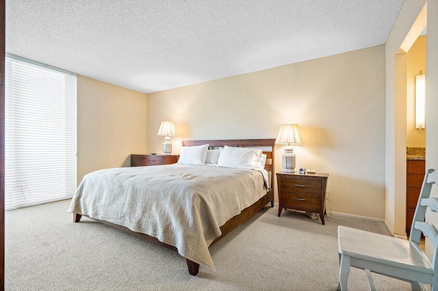 bedroom featuring light colored carpet, ensuite bath, and a textured ceiling