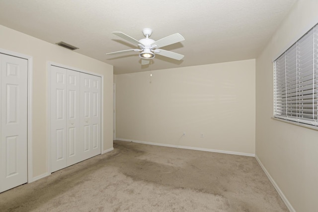 unfurnished bedroom with ceiling fan, light carpet, and two closets