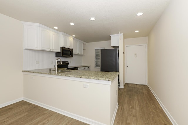 kitchen featuring white cabinets, light wood-type flooring, appliances with stainless steel finishes, light stone counters, and kitchen peninsula