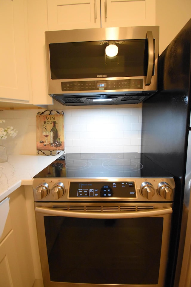 kitchen with white cabinetry, appliances with stainless steel finishes, tasteful backsplash, and light stone countertops