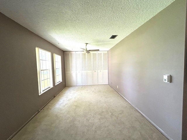 spare room featuring a textured ceiling, ceiling fan, and light colored carpet