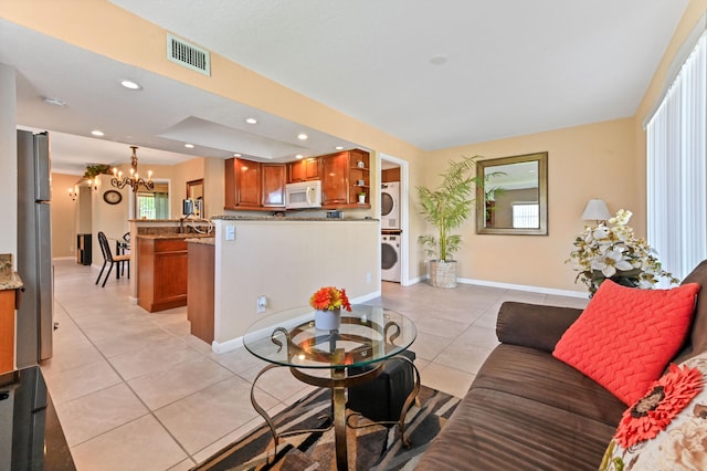 living room with light tile patterned floors, stacked washer and clothes dryer, and an inviting chandelier