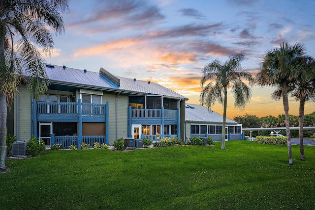 back house at dusk featuring a balcony, a lawn, and cooling unit