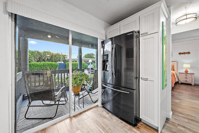 kitchen with light wood-type flooring, black fridge with ice dispenser, and white cabinets