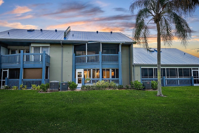 back house at dusk featuring a yard, a balcony, and central air condition unit