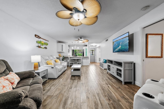 living room with a textured ceiling, wood-type flooring, and ceiling fan