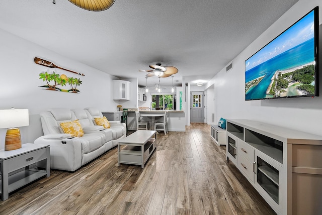 living room featuring dark wood-type flooring, ceiling fan, and a textured ceiling