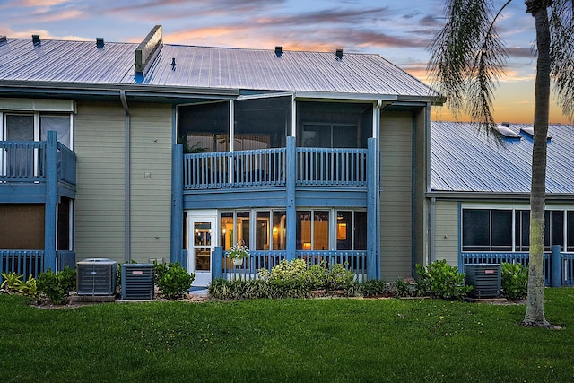 back house at dusk featuring a balcony, central air condition unit, and a lawn