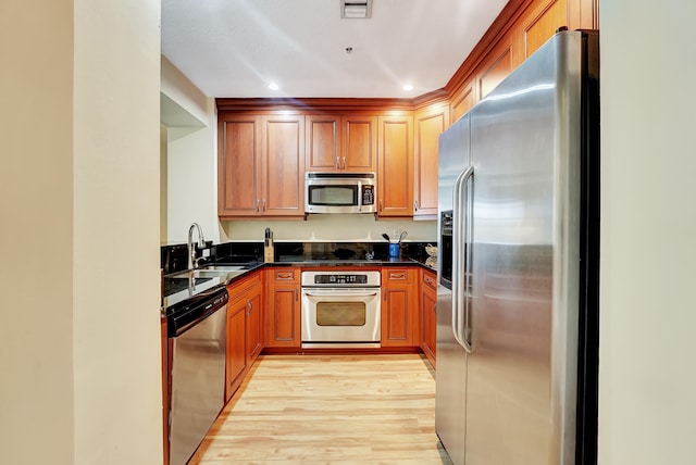 kitchen featuring light wood-type flooring, dark stone countertops, stainless steel appliances, and sink