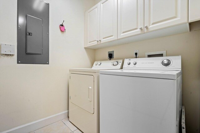 washroom featuring electric panel, cabinets, washer and clothes dryer, and light tile patterned flooring