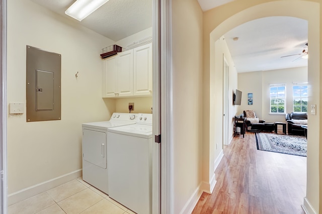 clothes washing area with cabinets, light hardwood / wood-style floors, electric panel, washing machine and dryer, and ceiling fan