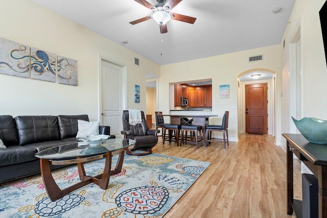 living room with a textured ceiling, ceiling fan, and light wood-type flooring