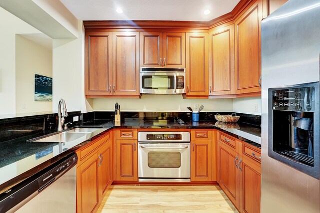 kitchen with dark stone countertops, light wood-type flooring, sink, and appliances with stainless steel finishes