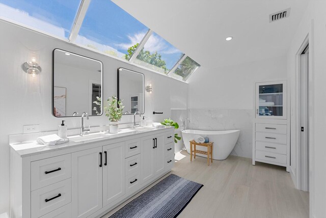 bathroom with vaulted ceiling with skylight, a bathing tub, vanity, wood-type flooring, and tile walls