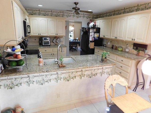 kitchen with ceiling fan, light stone countertops, kitchen peninsula, and black fridge