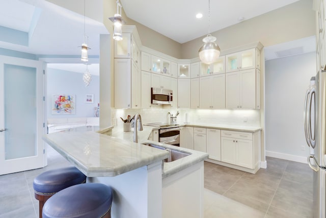 kitchen featuring decorative light fixtures, stainless steel appliances, kitchen peninsula, a kitchen breakfast bar, and tasteful backsplash