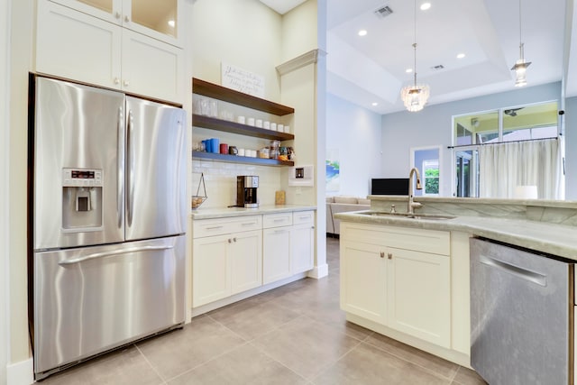 kitchen with light stone counters, sink, hanging light fixtures, a tray ceiling, and appliances with stainless steel finishes