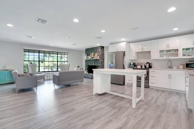 kitchen featuring a fireplace, light wood-type flooring, white cabinetry, and stainless steel appliances