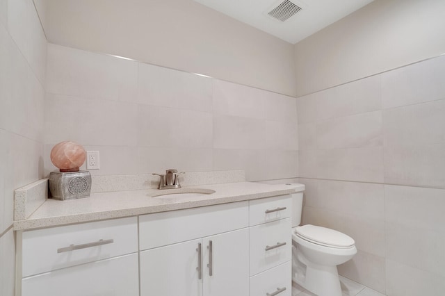 bathroom featuring tile patterned flooring, tile walls, toilet, and vanity