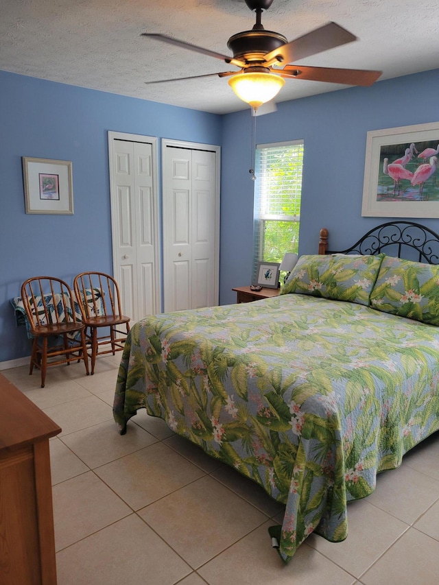 tiled bedroom featuring multiple closets, ceiling fan, and a textured ceiling