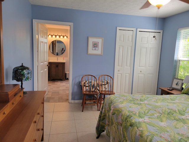 bedroom featuring connected bathroom, ceiling fan, multiple closets, a textured ceiling, and light tile patterned flooring