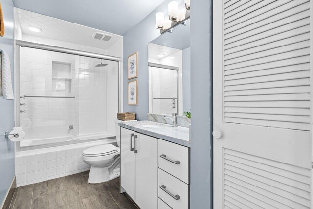 full bathroom featuring shower / bath combination with glass door, vanity, toilet, and hardwood / wood-style floors