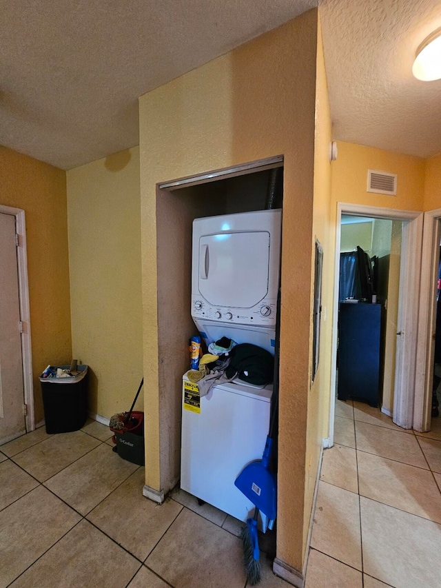 washroom with a textured ceiling, stacked washer / dryer, and light tile patterned flooring