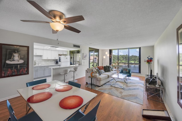 dining room featuring baseboards, ceiling fan, light wood-style flooring, and a textured ceiling