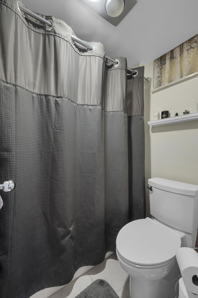 bathroom featuring toilet, a shower with curtain, and tile patterned floors