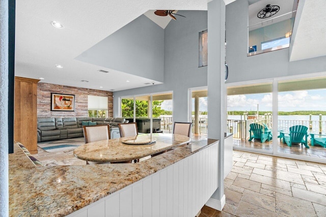 interior space with a high ceiling, ceiling fan, and light stone counters