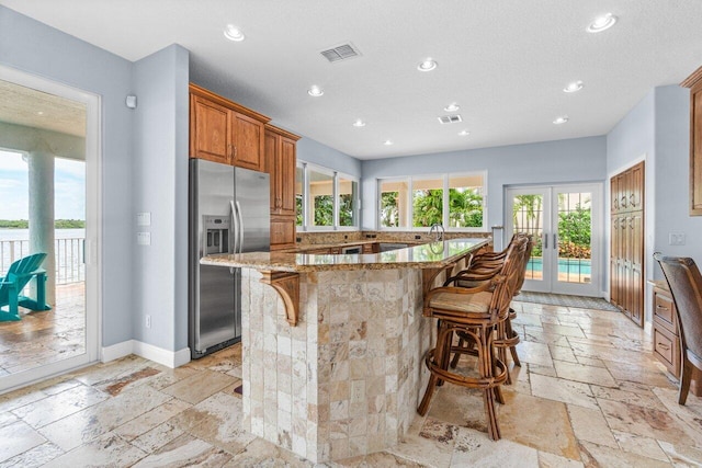 kitchen featuring a kitchen bar, a spacious island, stainless steel fridge with ice dispenser, french doors, and light stone counters