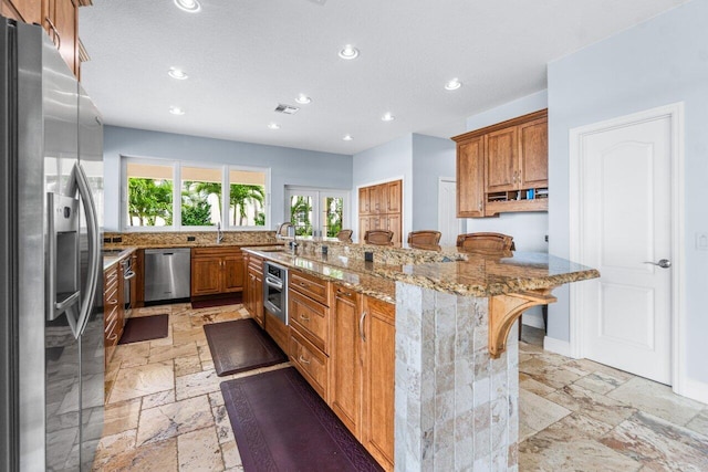 kitchen featuring light stone countertops, appliances with stainless steel finishes, sink, a breakfast bar, and a center island with sink