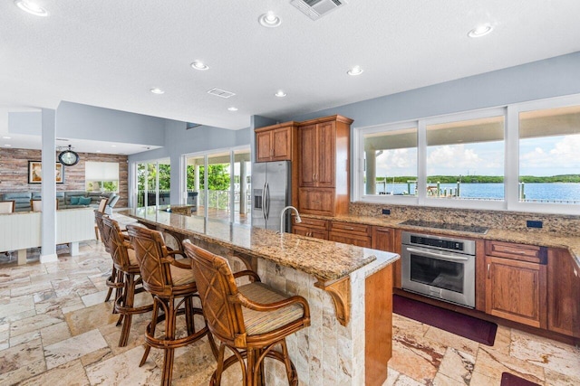 kitchen featuring sink, a water view, light stone counters, a kitchen bar, and stainless steel appliances