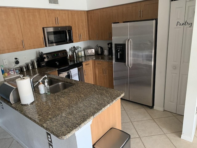 kitchen featuring visible vents, dark stone countertops, appliances with stainless steel finishes, a peninsula, and light tile patterned flooring