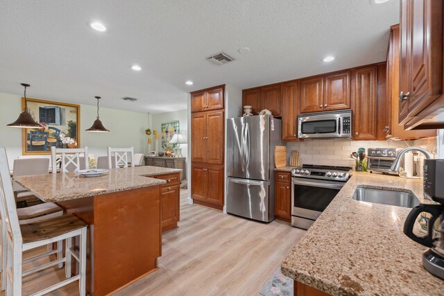 kitchen with light hardwood / wood-style flooring, light stone counters, stainless steel appliances, and sink