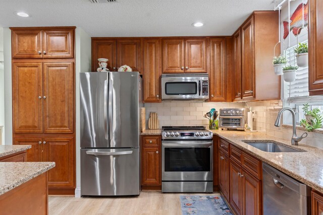 kitchen featuring light hardwood / wood-style flooring, light stone counters, sink, and appliances with stainless steel finishes