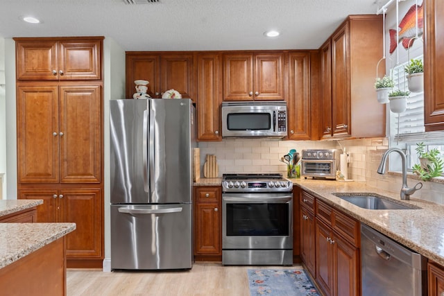 411 Sandpiper Dr Unit A, Fort Pierce, FL 34950 - kitchen featuring brown cabinets, light wood finished floors, appliances with stainless steel finishes, a sink, and light stone countertops