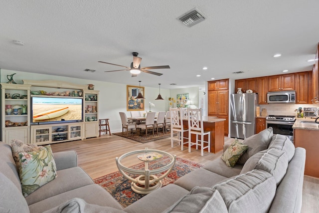 living room with a textured ceiling, ceiling fan, and light hardwood / wood-style floors