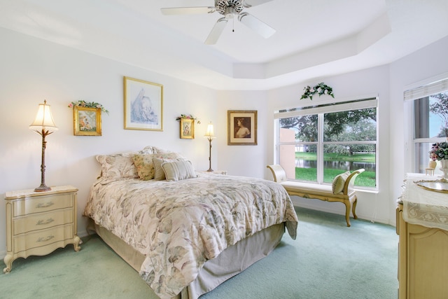 carpeted bedroom with ceiling fan and a raised ceiling