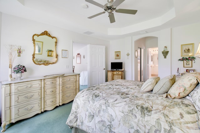 bedroom featuring ceiling fan, carpet floors, a raised ceiling, and ensuite bath