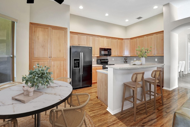 kitchen featuring a kitchen bar, light wood-type flooring, tasteful backsplash, black appliances, and a kitchen island