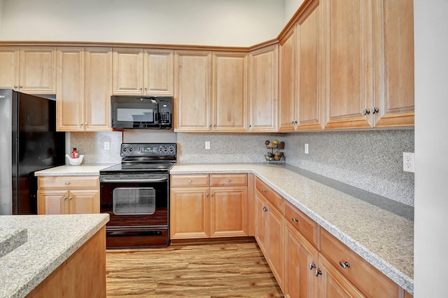 kitchen with decorative backsplash, light brown cabinetry, light wood-type flooring, light stone counters, and black appliances