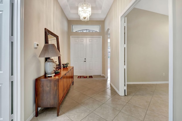 tiled entryway featuring a raised ceiling, plenty of natural light, and a notable chandelier