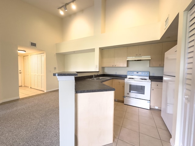 kitchen with white appliances, light carpet, track lighting, kitchen peninsula, and a towering ceiling