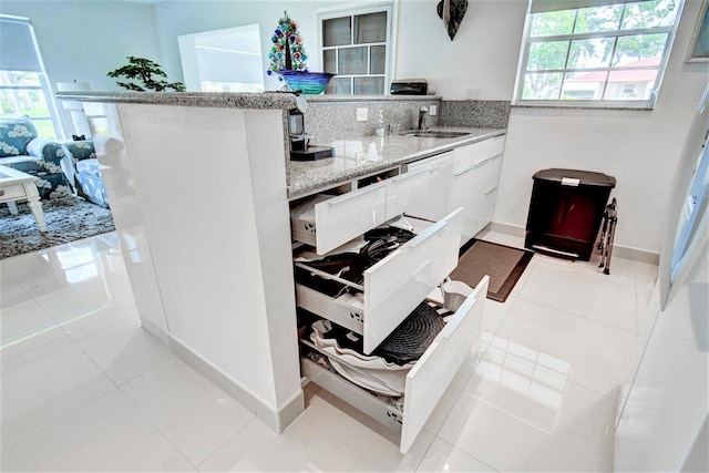 kitchen with white cabinets, light tile patterned floors, dishwasher, light stone countertops, and sink