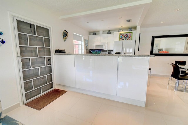 kitchen featuring fridge with ice dispenser, light stone counters, and white cabinets