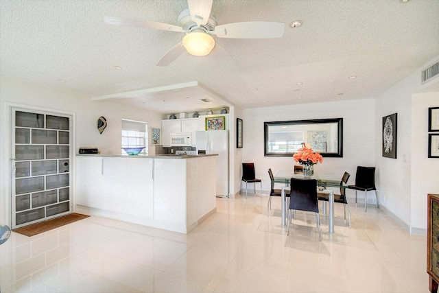 kitchen featuring a textured ceiling, white appliances, light tile patterned floors, kitchen peninsula, and white cabinetry